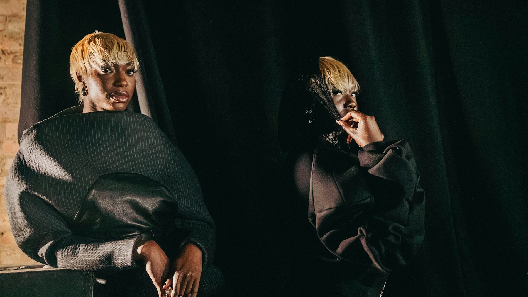 Two styled figures in dark editorial looks under dramatic side light
